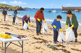 On a sunny beach, volunteers in yellow gloves fill white sacks with litter, a child working next to an adult; a harbour wall and moored boats are behind, and a table holds spare gloves and pickers.