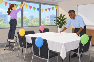 Two colleagues decorate a meeting room: one hangs a string of paper flags, and the other spreads a white cloth on the table among plain balloons.